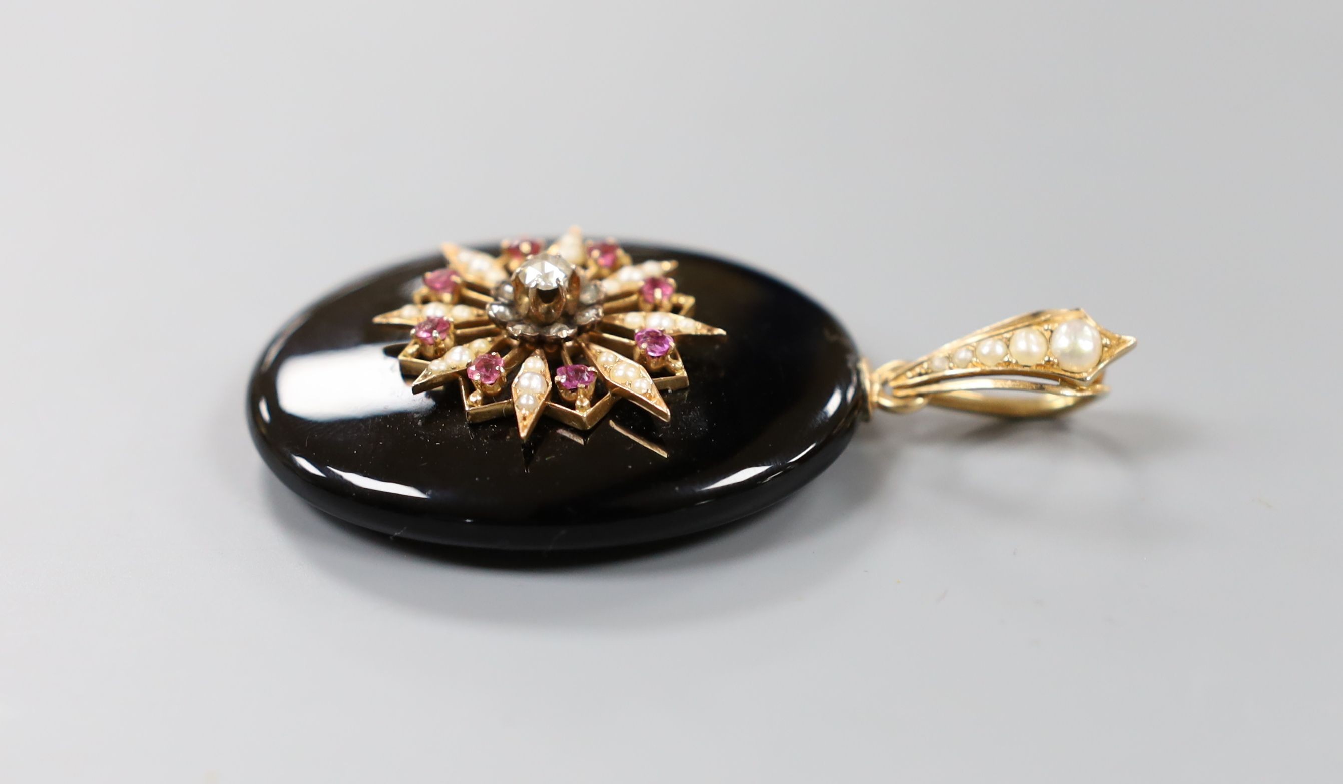 A Victorian black enamel, rose cut diamond, ruby coloured paste and seed pearl set oval mourning pendant, with glazed back and seed pearl set yellow metal bale, overall 69mm.